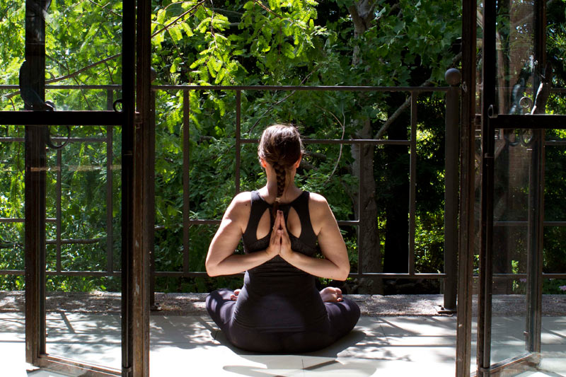 Petaluma_Spa_McEvoy_Ranch_Yoga Woman in workout clothes pressing her hands together behind her back on a terrace with a view of trees.