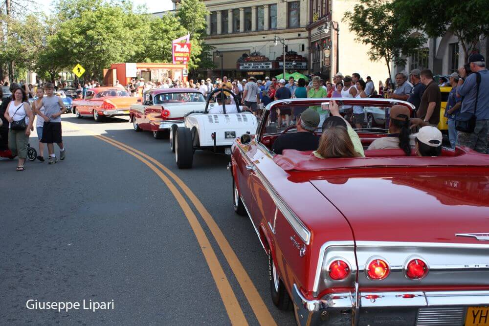 Red convertible in line with classic cars cruising historic downtown