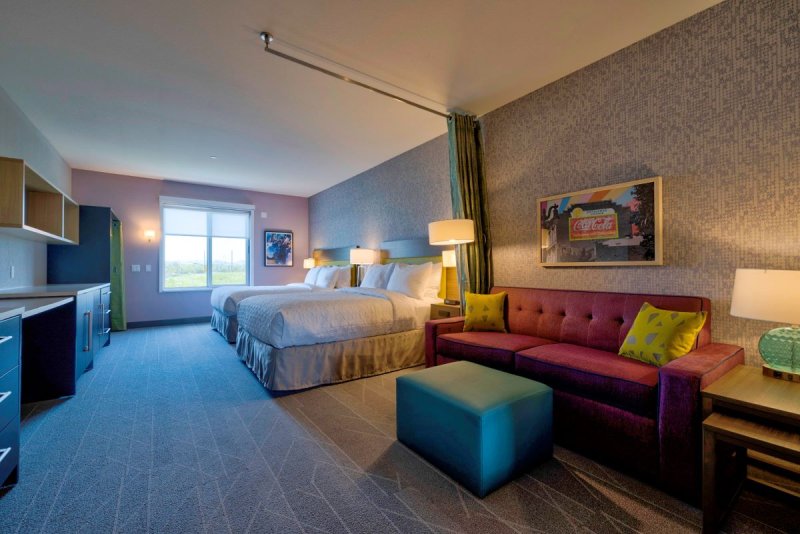 Room photo with bed, sitting area, lamps on. Brightly colored.