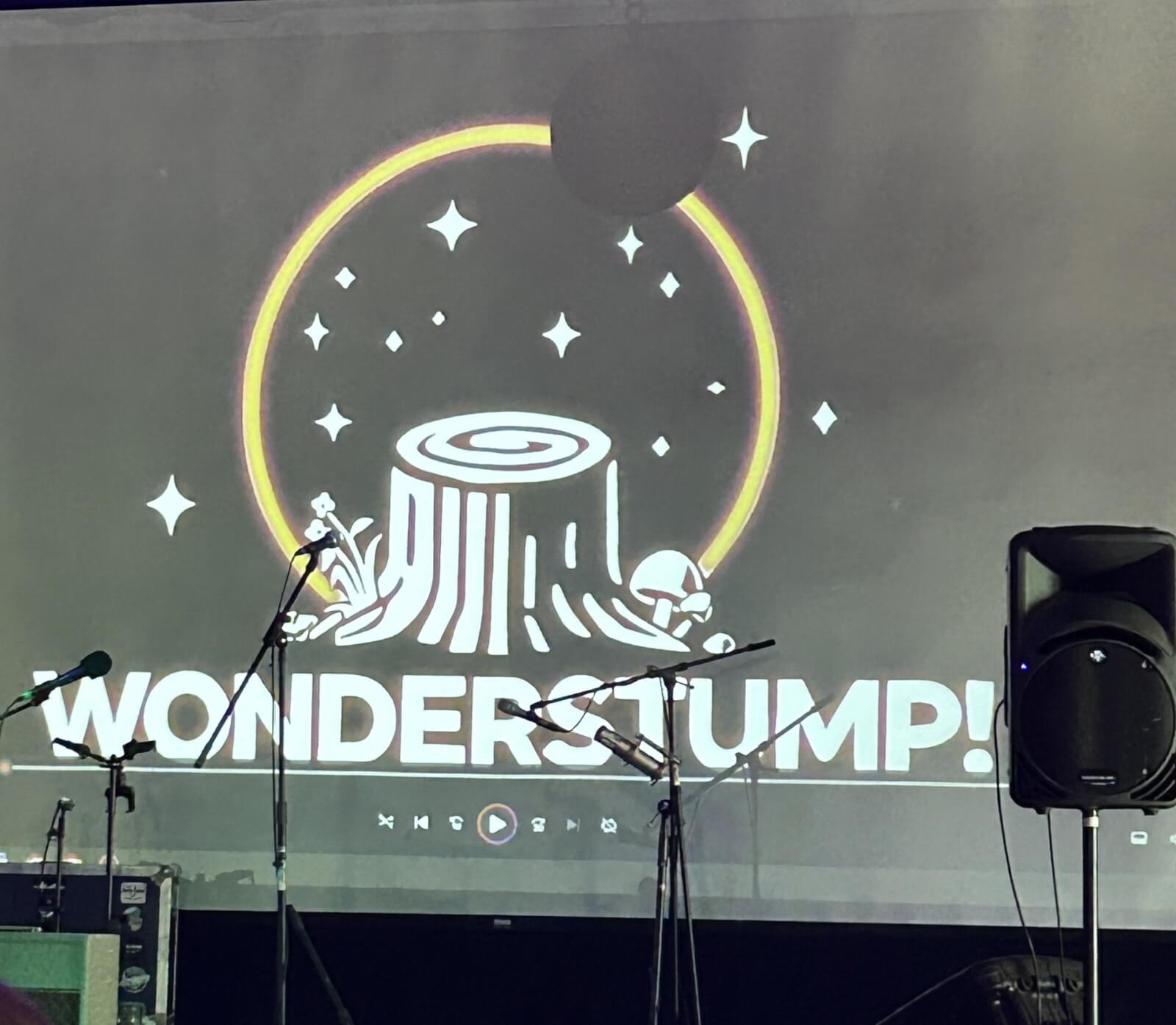 Logo featuring a tree stump design on screen behind mic stands