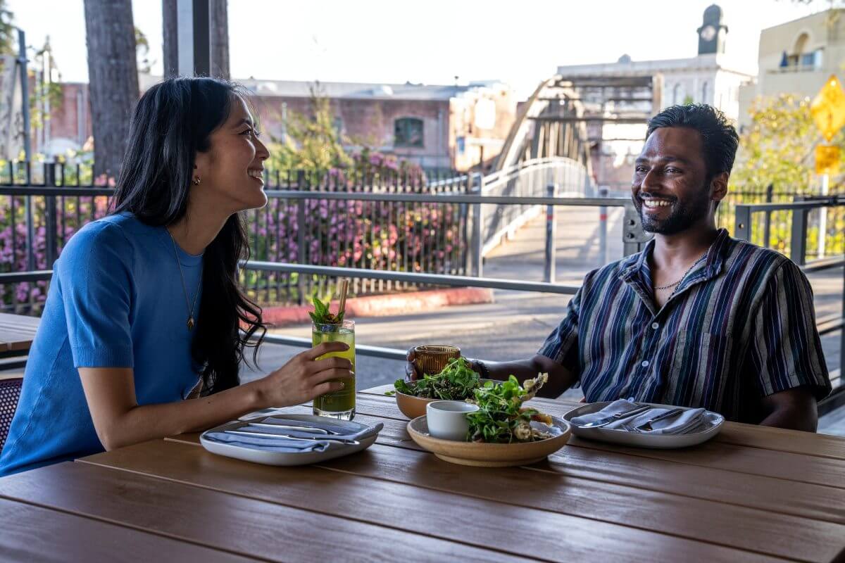 Multiracial couple enjoying outdoor meal at restaurant. Footbridge in background