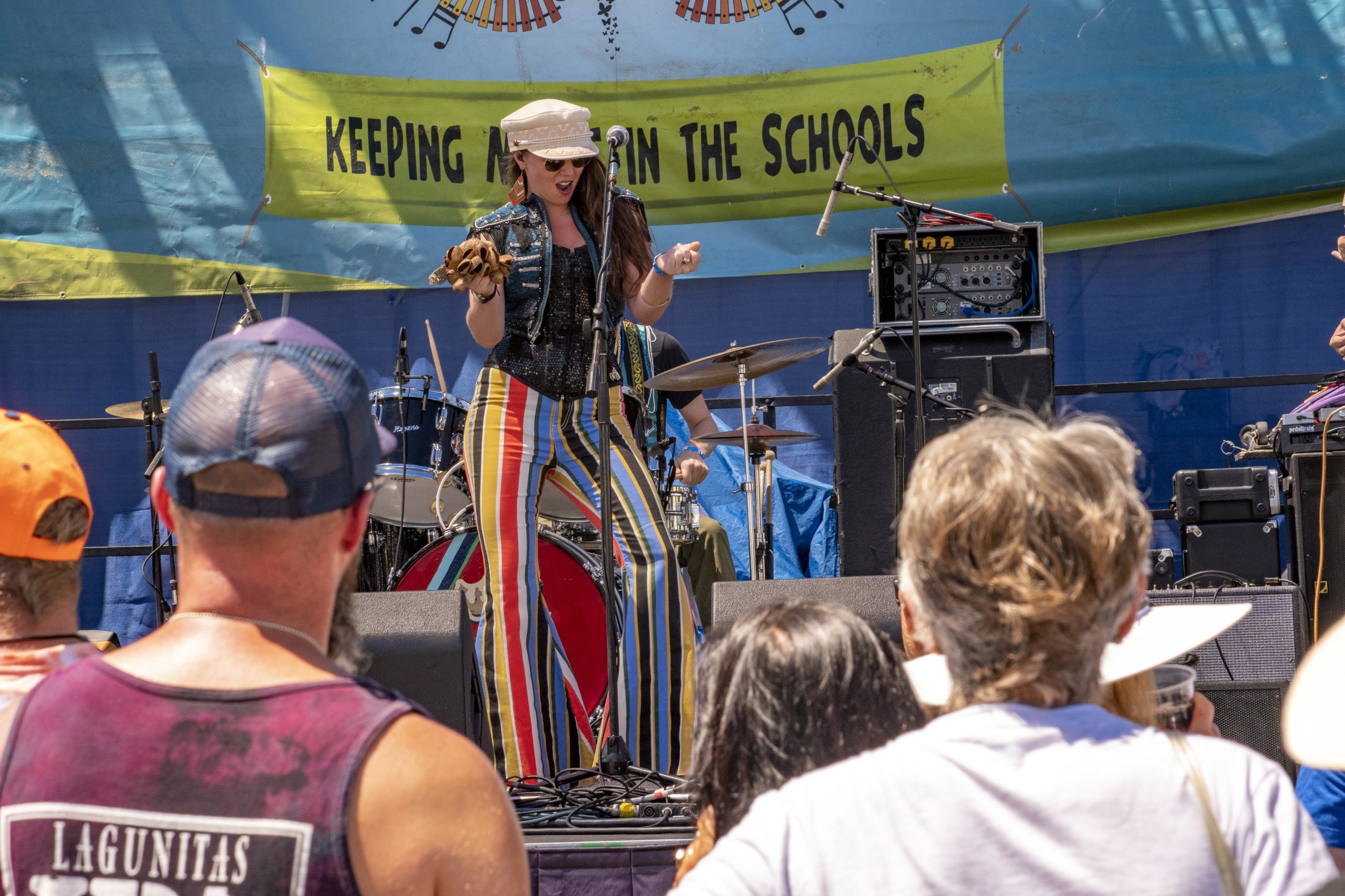 Woman in striped pants performing on outdoor stage with tambourine at music festival.