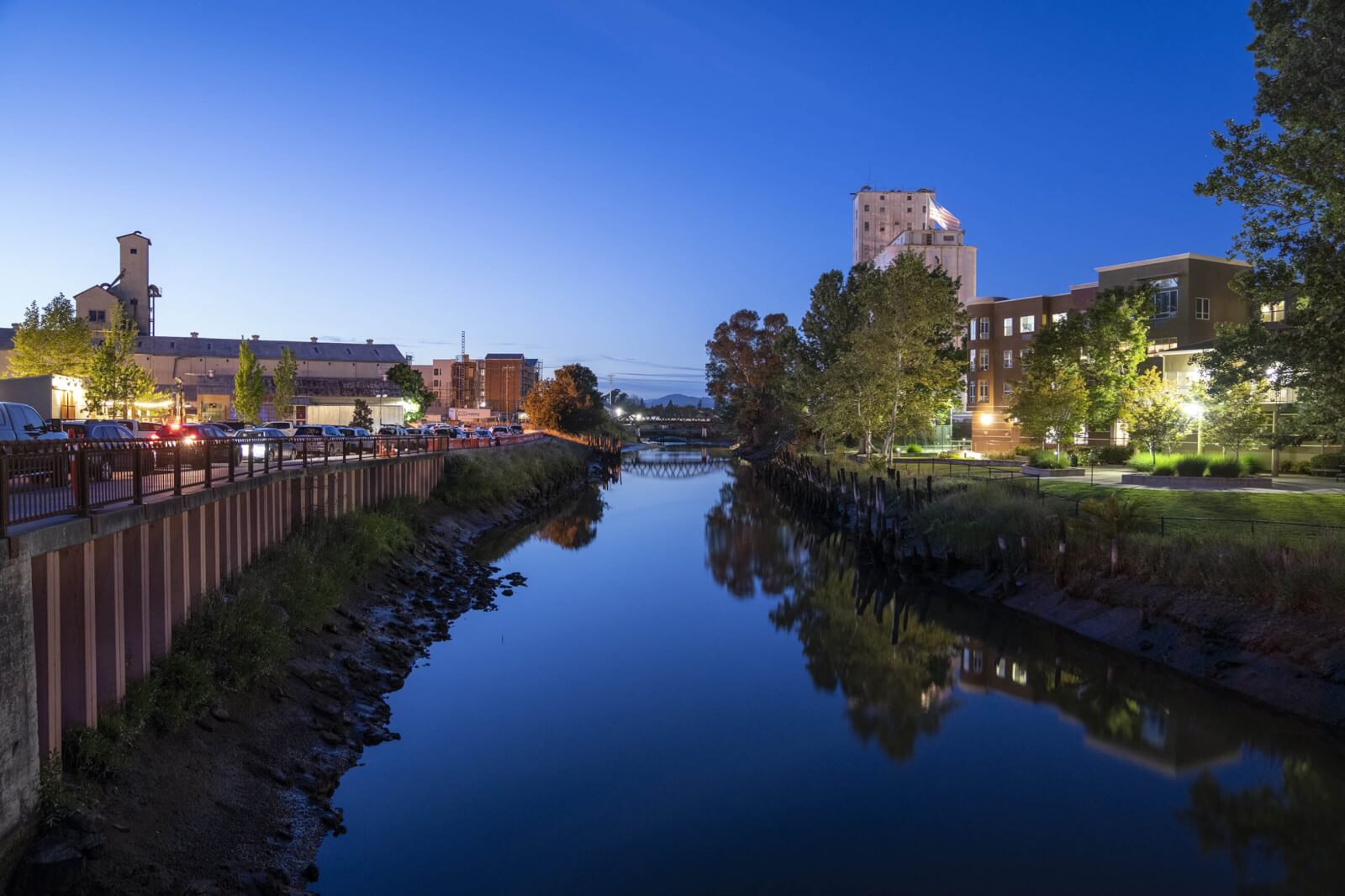 evening on river with lighted buildings on either side and bridge in distance