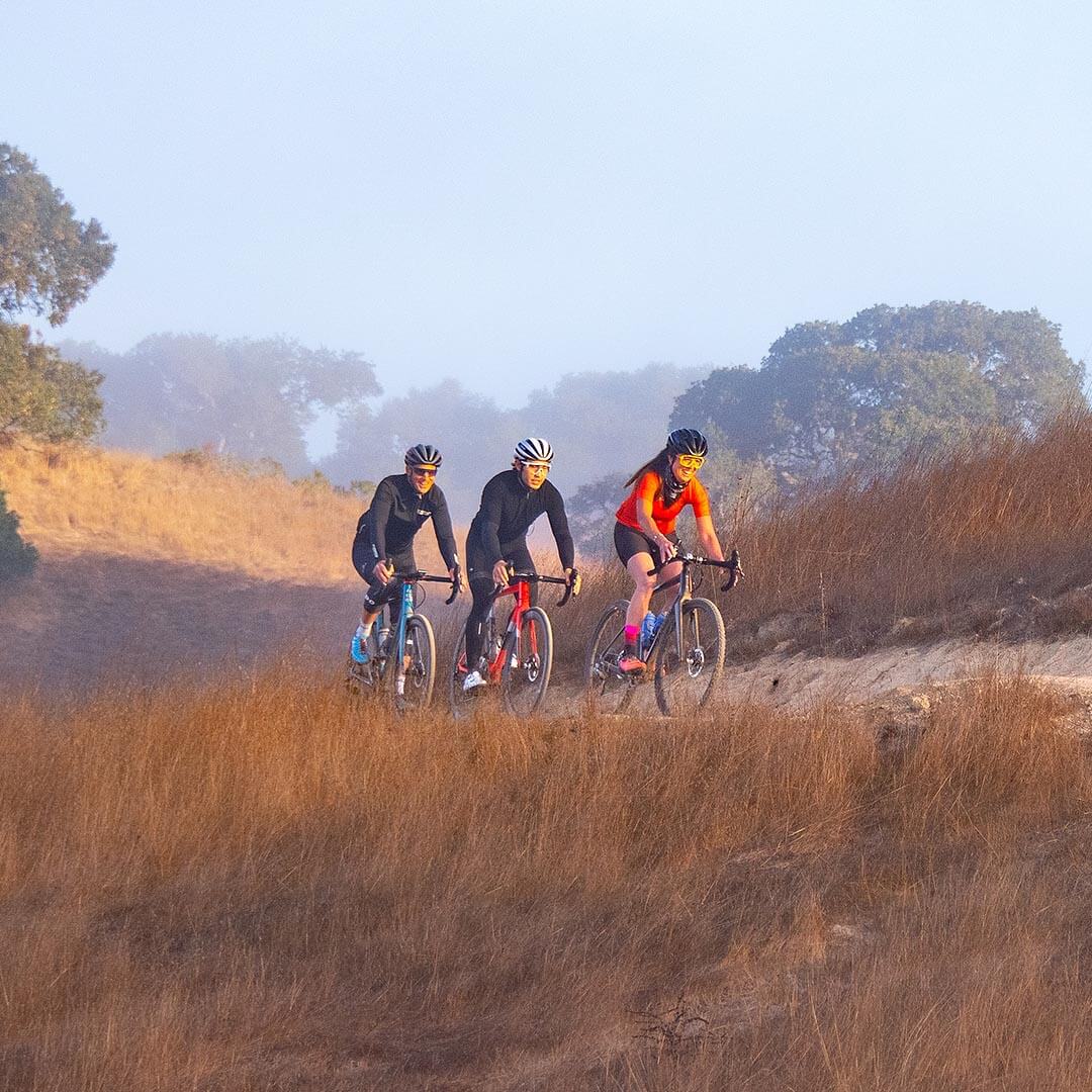 Three cyclists in cycle gear on hillside trail in the fog.