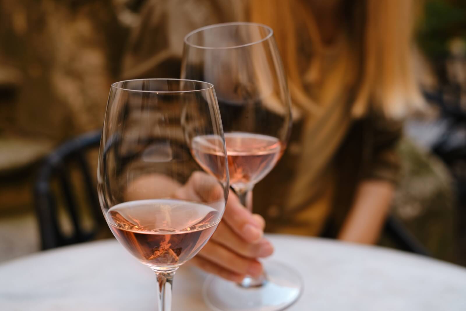 Wine tasting with petaluma style 1 Two glasses of rosé wine on white tablecloth, woman's hand holding one by stem.