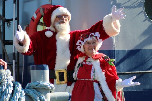 Santa with arms outstretched in greeting with Mrs Claus on tugboat