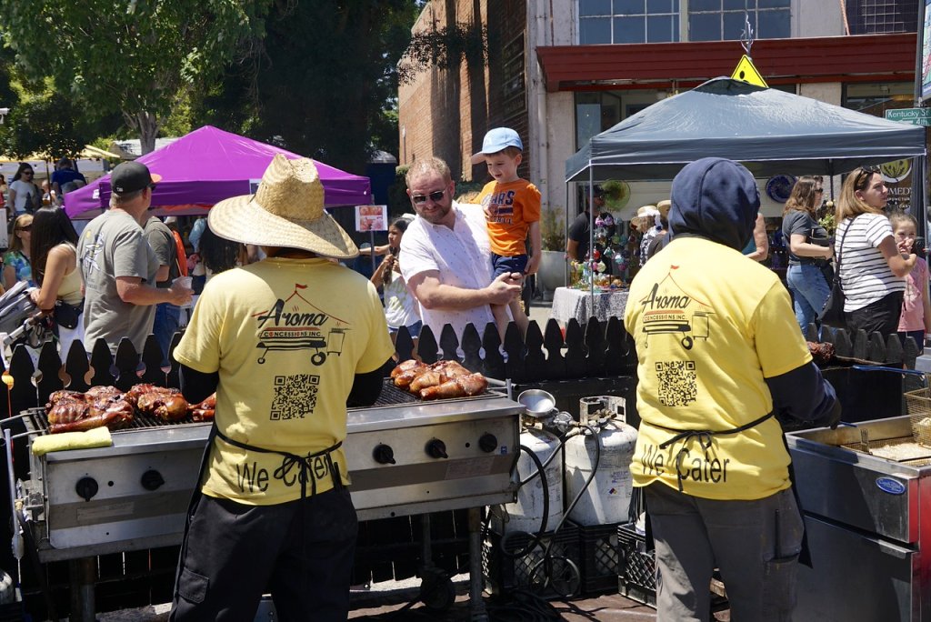Food vendors in yellow shirts at a festival barbecuing meat