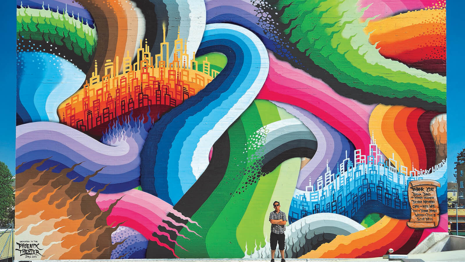 Man in shorts with arms folded in front of colorful mural outside Phoenix Theater