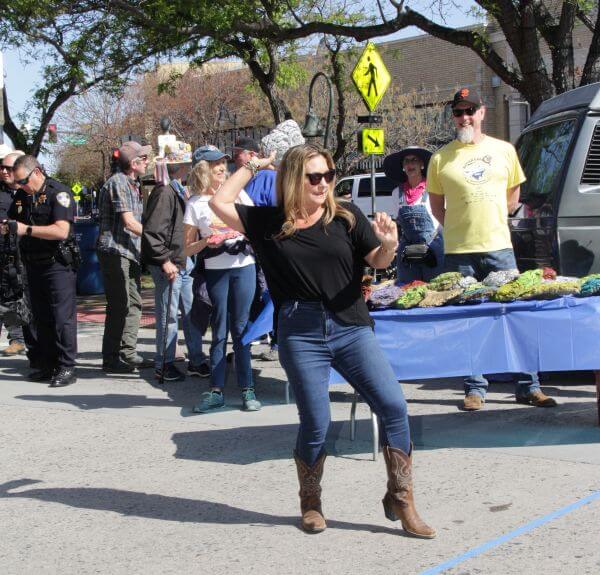 Woman in cowboy boots tossing a cow chip with a table full of painted cow chips behind her
