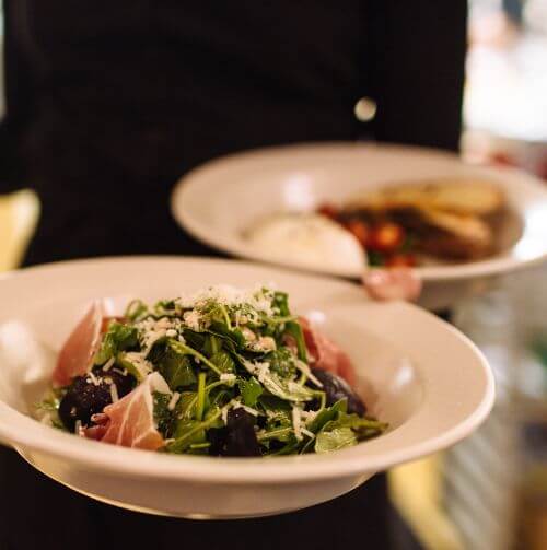 Two plates held by a waitperson's hand, one with salad.