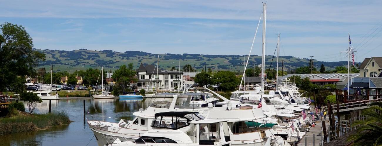 Boats docked in the petaluma turning basin with a historic building and green hills across river