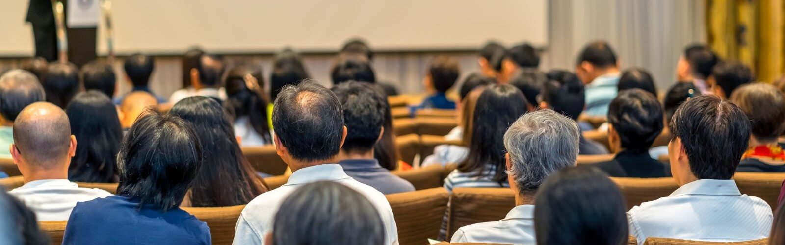 People seated in an auditorium. View from seat toward rear - backs of heads.