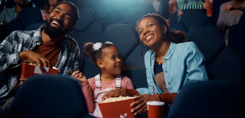 Family of 3 enjoying a movie and popcorn at theater.