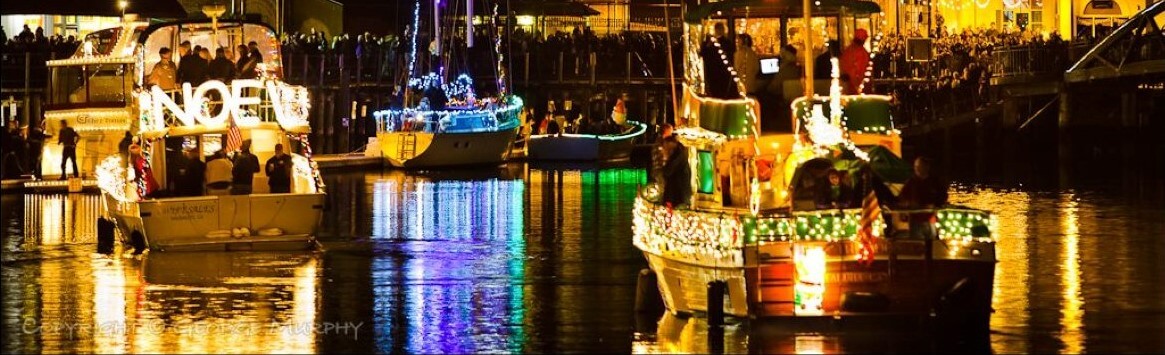 Night on a river with boats decked out in holiday lights with reflections off the water