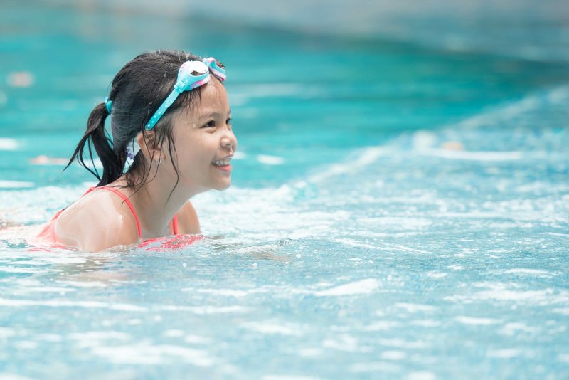Smiling asian girl with goggles on head in pool.