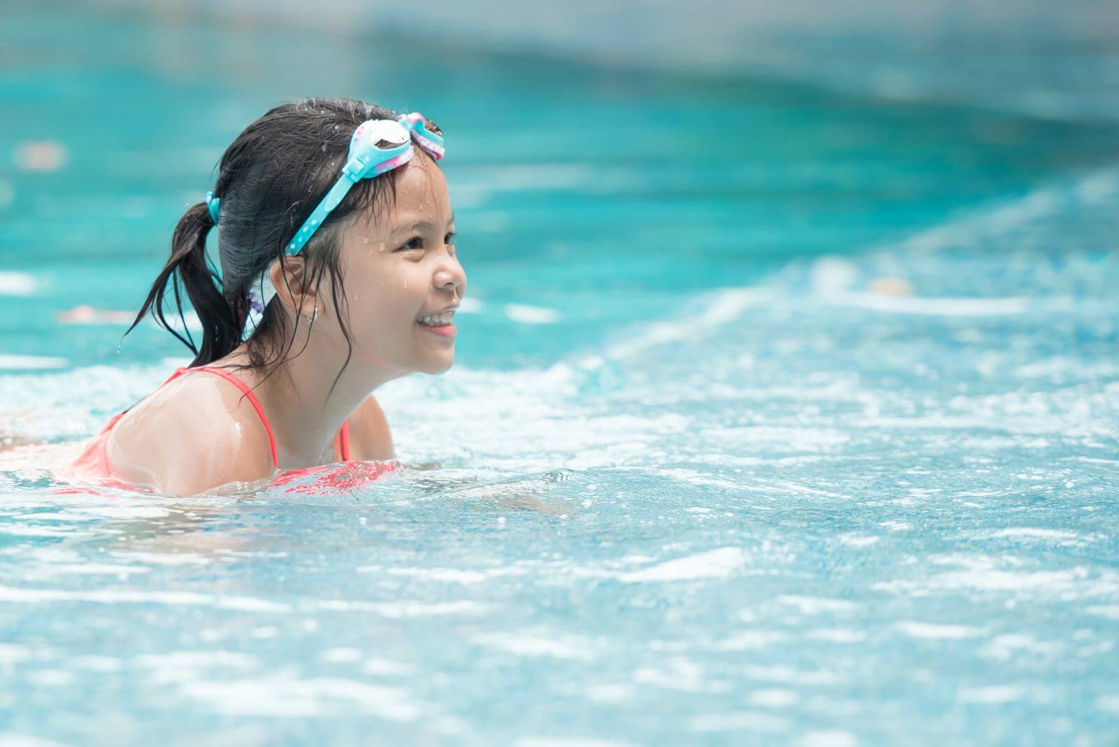 Smiling asian girl with goggles on head in pool.