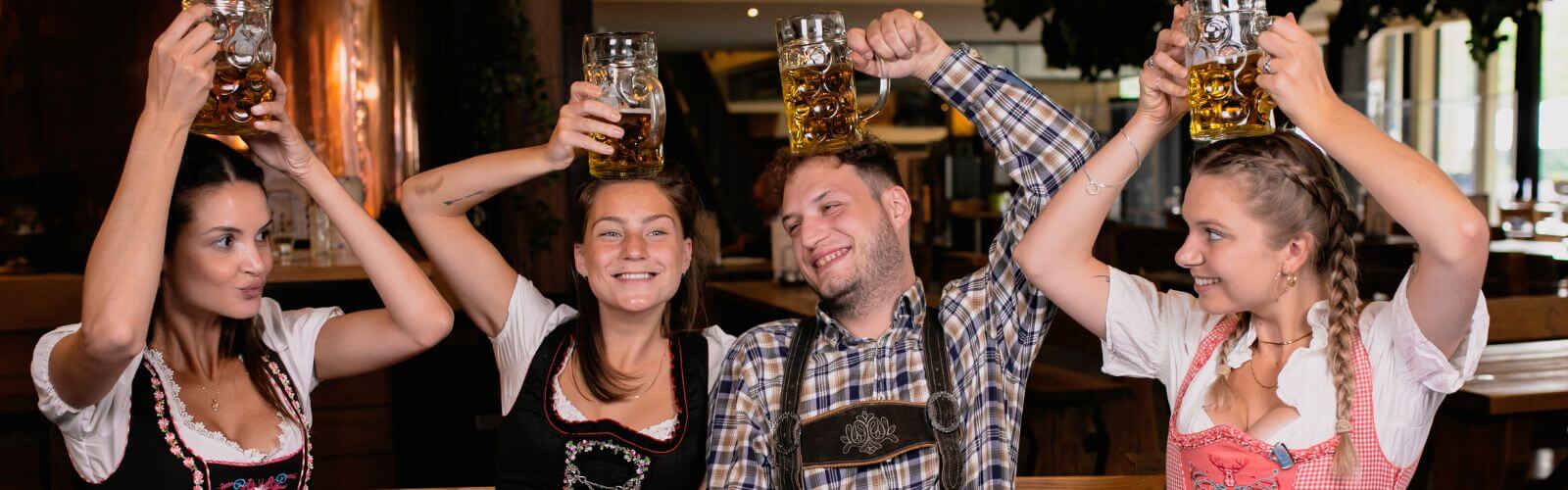 Four adults in octoberfest costumes holding up glass mugs of beer