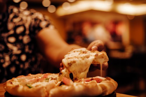 Person pulling cheesy slice from pizza