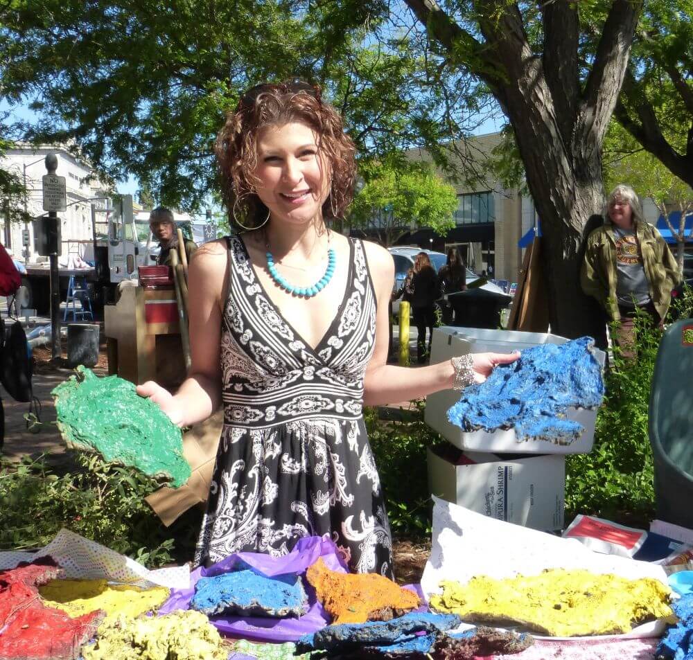 Woman holding painted cow chips in front of table full of them