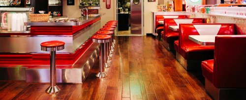 A vintage-style diner booth with red vinyl seats, a white tabletop, and chrome accents, evoking a classic mid-century café atmosphere.
