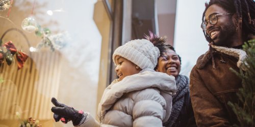 African American family of three holiday shopping. Dad has tree, daughter pointing at display window.
