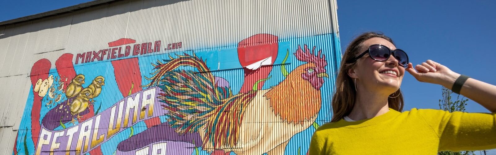Woman in sunglasses smiling in front of petaluma chicken mural